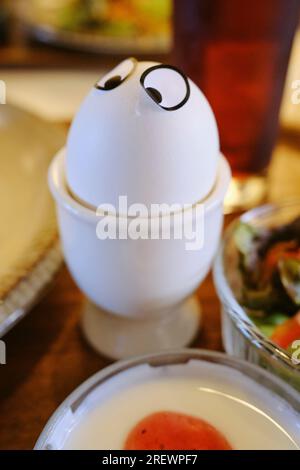 July 2023, A boiled egg with cute eye stickers in a cup as part of a morning breakfast set Stock Photo