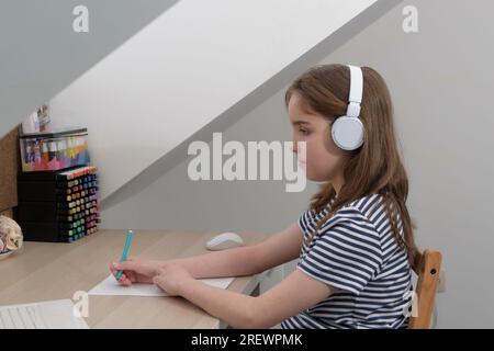 Learn a foreign language audio. Girl schoolgirl doing homework online. Sound through headphones Stock Photo