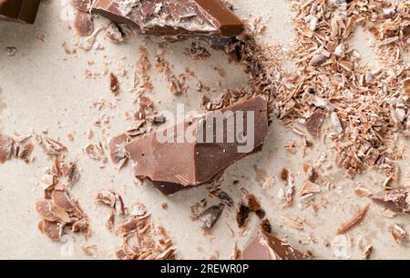 pieces of chocolate randomly scattered on the table, broken and crumbled natural chocolate, edible milk chocolate made from cocoa and sugar Stock Photo