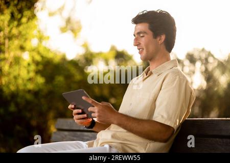 Young man digital nomad sitting on bench, using tablet Stock Photo