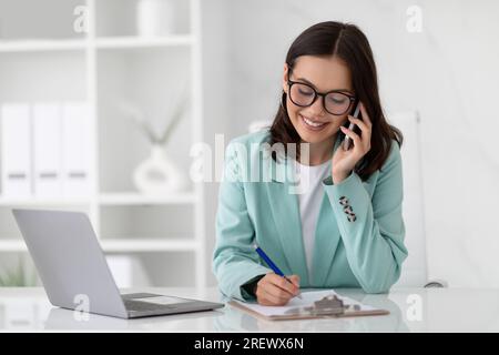 Glad young caucasian businesswoman in suit and glasses with computer calling by phone Stock Photo