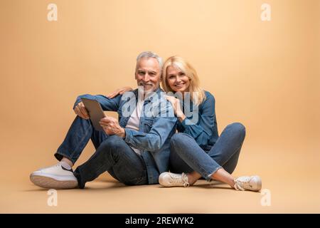 Positive senior spouses using digital tablet, beige background Stock Photo