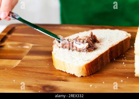 child with chocolate paste and a loaf, a child prepares sweets in the kitchen from a roll and chocolate, chocolate butter that the child puts on a loa Stock Photo