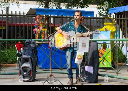 Niteroi, Brazil, A street musician or artist plays the guitar and sings on an outdoors market or fair. The performer has his music instrument connecte Stock Photo