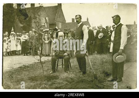 Original WW1 era postcard of a poignant village scene - a group of villagers are watching the planting of the peace tree on 19 July 1919 for the National Celebration of Peace day. There are servicemen in background, a  sad old man is  sitting next to the tree, the village dignitary or perhaps a father who had lost several sons in the war, behind him a crying girl with hanky. So much loss. The crowd hold banners & British Union Jack flags, French Tricolor flags hangs from a window - perhaps in support of the treaty of Versailles signed in June 1919 - the official ending of the war.  U.K. Stock Photo