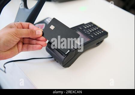 Selective focus. Hand holding black mockup plastic card with copy advertising space over credit card reader, shopping, making cashless payment in the Stock Photo