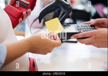 Close-up hands of a customer swiping a mockup golden credit card, making contactless payments. Paying goods using online internet banking, NFC technol Stock Photo