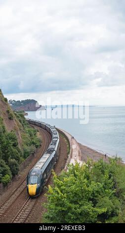 Devon, England – July 21, 2023: A Great Western Railway passenger train from London Paddington on the atmospheric route along the coast  at Teignmouth Stock Photo