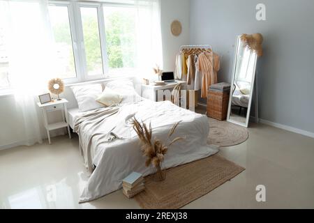 Interior of children's bedroom with cozy bed, laptop and clothes hanging on rack Stock Photo