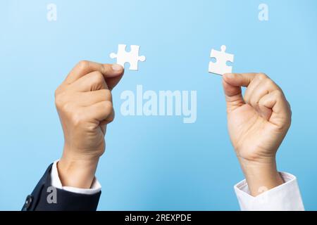 Two hands trying to connect couple puzzle piece on blue background. Teamwork concept. Closeup hand of connecting jigsaw puzzle. Stock Photo