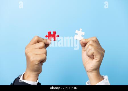 Two hands trying to connect couple puzzle piece on blue background. Teamwork concept. Closeup hand of connecting jigsaw puzzle. Stock Photo