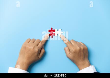 Two hands trying to connect couple puzzle piece on blue background. Teamwork concept. Closeup hand of connecting jigsaw puzzle. Stock Photo