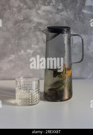 Glass misted decanter and a glass with cold fruit drink on a white kitchen table Stock Photo