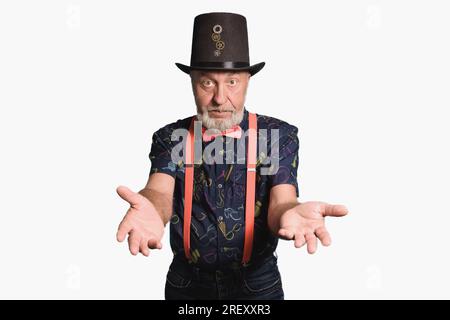 Old man in a festive costume in a cylinder hat with a pink bow tie and suspenders invites you to a holiday. Concept - tricks Stock Photo