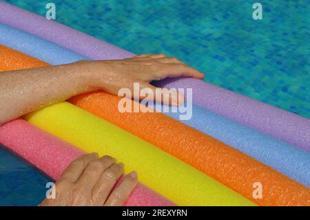 Rainbow coloured floating foam sticks and female hands, in swimming pool Stock Photo