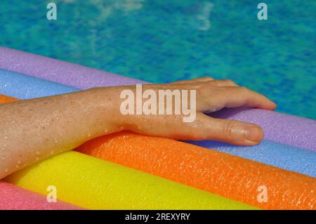 Rainbow coloured floating foam sticks and female hand, in swimming pool Stock Photo