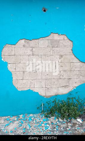 cracked surface of the blue wall with bricks in wall visible Stock Photo