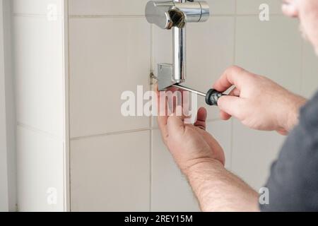 Removing screws of the shower holder from the wall in the bathroom. Stock Photo