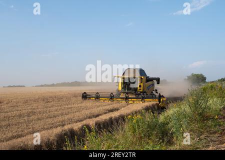 Harvester working on a wheat fields near ongoing Ukrainian counter-offensive. Despite the currently ongoing Ukrainian counteroffensive in the Zaporizhzhya region, and the risk of a terrorist attack on the nuclear power plant, daily life in the Zaporizhzhia region is still going on. Warm evenings fill the city's streets with strolling people, while sunflowers are blooming in the frontline areas and the first harvests has begun. However, intensified warfare does not let up - intense shelling almost daily takes the lives of people, who additionally suffer from lack of water after the Nova Kakhovk Stock Photo