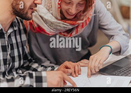 A shot of female employee wearing hijab explaining graph charts on paper, helping her male colleague at the office Stock Photo