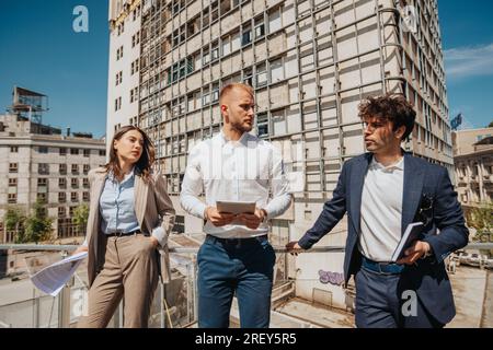 Three young architects discussing project leaning on a metal fence in the city, project development, construction site Stock Photo