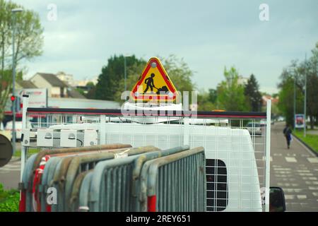 Road repair sign with flashing lights on a special vehicle, in the cargo area of a section of a metal safety fence. In the background, cars and people Stock Photo
