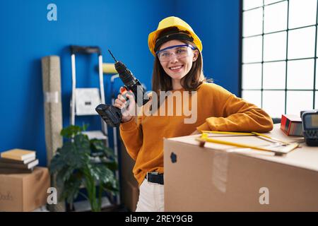 Young blonde woman wearing hardhat holding drill at new home Stock Photo