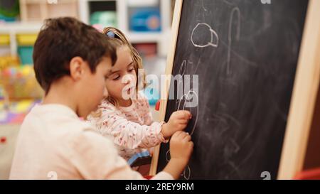 Adorable boy and girl preschool students drawing on blackboard at kindergarten Stock Photo