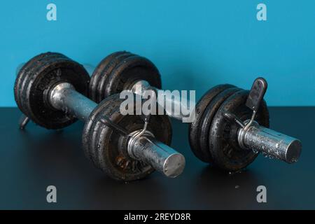 A pair of wet rusty dumbbells indoors on a table. close-up. blue background Stock Photo