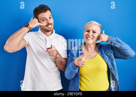 Young brazilian mother and son standing over blue background smiling doing talking on the telephone gesture and pointing to you. call me. Stock Photo