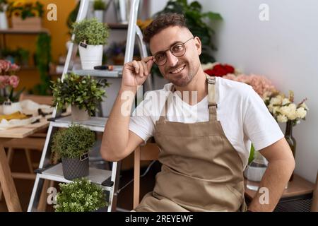 Young hispanic man florist smiling confident sitting on chair at flower shop Stock Photo