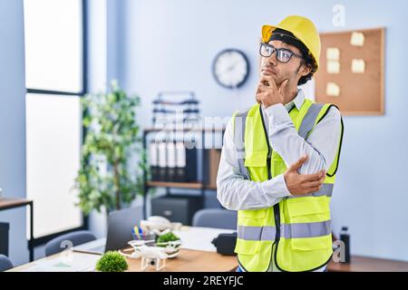 Hispanic man wearing architect hardhat thinking concentrated about doubt with finger on chin and looking up wondering Stock Photo