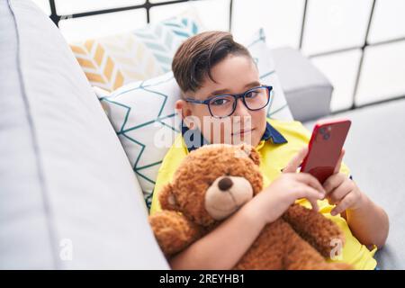 Adorable hispanic boy using smartphone hugging teddy bear at home Stock Photo