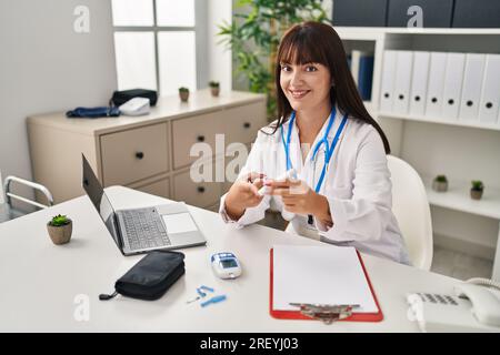 Young beautiful hispanic woman doctor smiling confident measuring glucose at clinic Stock Photo
