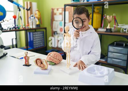 Adorable hispanic girl scientist student using magnifying glass at laboratory classroom Stock Photo