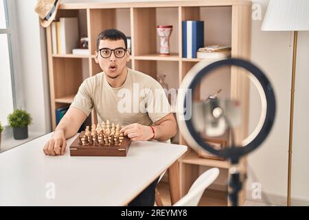 Young arab man doing chess tutorial scared and amazed with open mouth for surprise, disbelief face Stock Photo