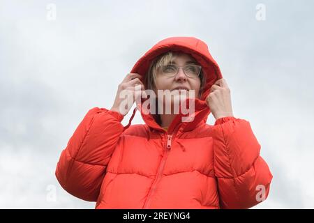 Portrait of a woman in a red jacket with a hood on her head against a cloudy sky Stock Photo