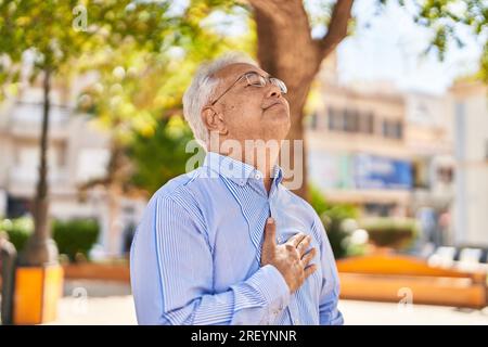Senior man touching heart with worried expression at park Stock Photo