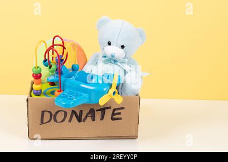 Donation, charity concept. Toy donation box with teddy bear, wooden and plastic educational toys on white desk Stock Photo