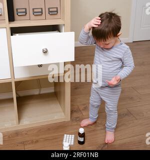 Toddler baby opened the cabinet drawer with pills and medicine. Child boy holding a pack of pills in the home living room. Kid age one year nine month Stock Photo