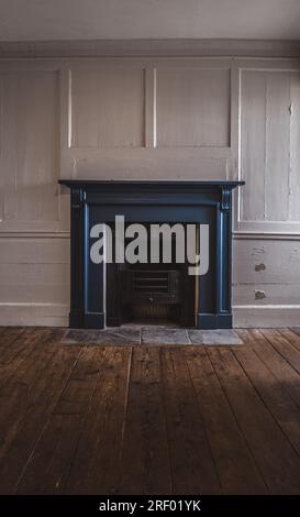 An unused and unlit old coal fireplace in a run down home interior with flaking paint on panelled walls during the global energy crisis with rising fu Stock Photo
