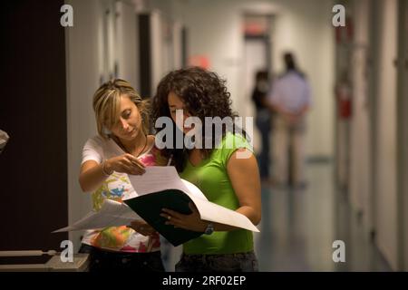 Two individuals review documents in a well-lit hallway, engaging in a discussion. Stock Photo