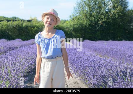 A young girl stands in a blooming lavender field. Straw hat, blue shirt Stock Photo