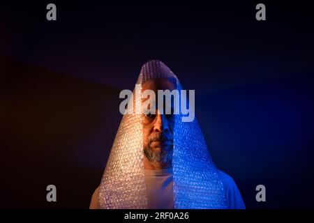 Bald man with a beard, with bubble wrap around his head. Isolated on dark red background. Stock Photo