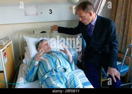 A hospital patient in bed converses with a standing visitor dressed in a suit. Stock Photo