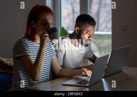 Young modern freelancing couple sitting at table in living room working from home together Stock Photo