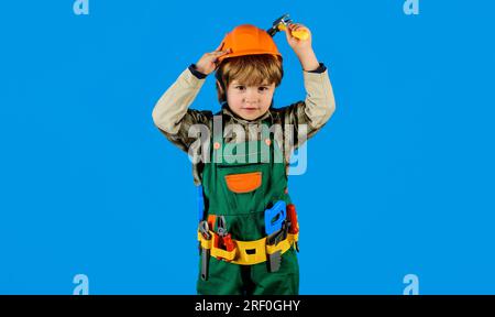 Little child repairman in builder uniform with toolbelt and hammer. Small kid boy in hardhat and overalls with hammer. Builder boy in safety helmet Stock Photo