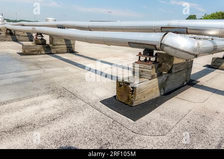 Roof mounted industrial insulated HVAC pipes on gray roof and wooden supports. Stock Photo