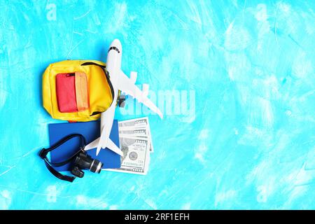 Traveling by plane: Toy airplane model, vibrant backpack, passport with cash and tiny camera placed on a light blue background. Stock Photo