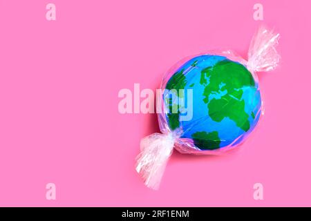 Miniature globe wrapped in plastic, resembling a candy. Global issue of plastic pollution and waste on our environment. Stock Photo